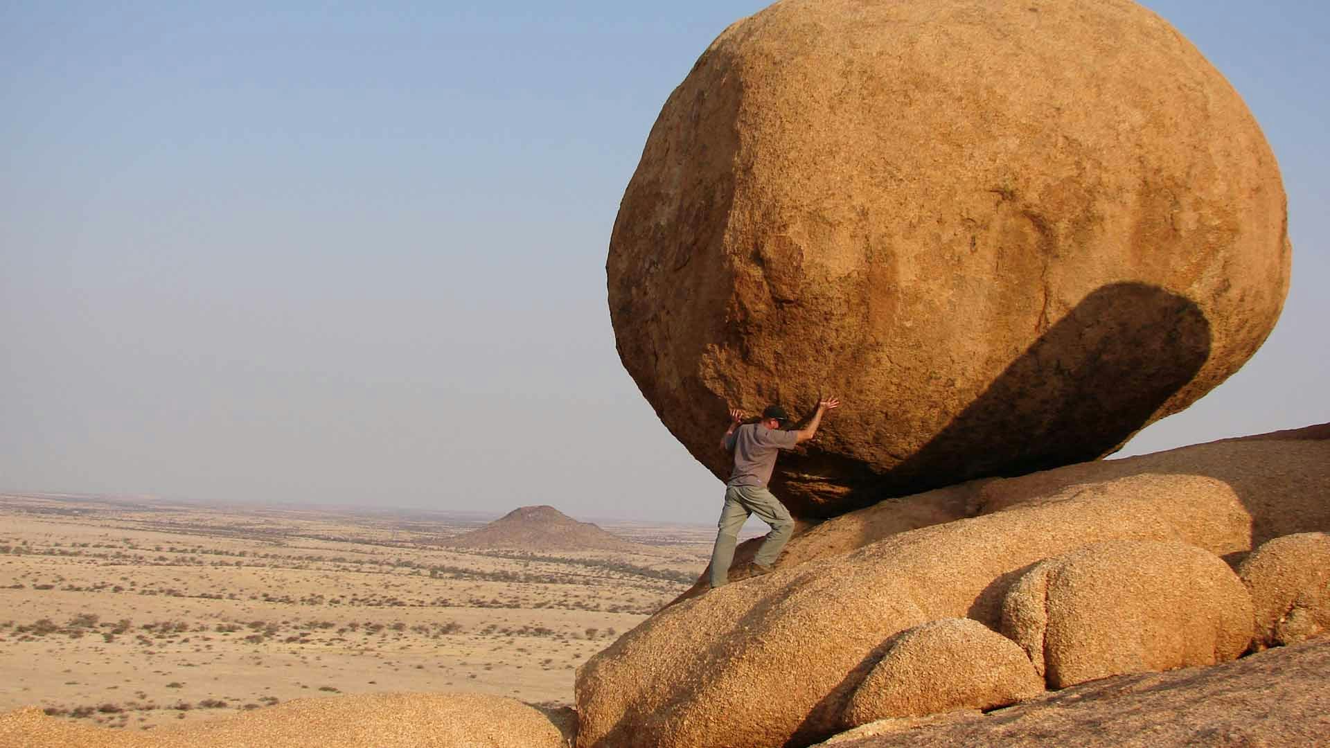 Man Pushing Up Bolder in Desert